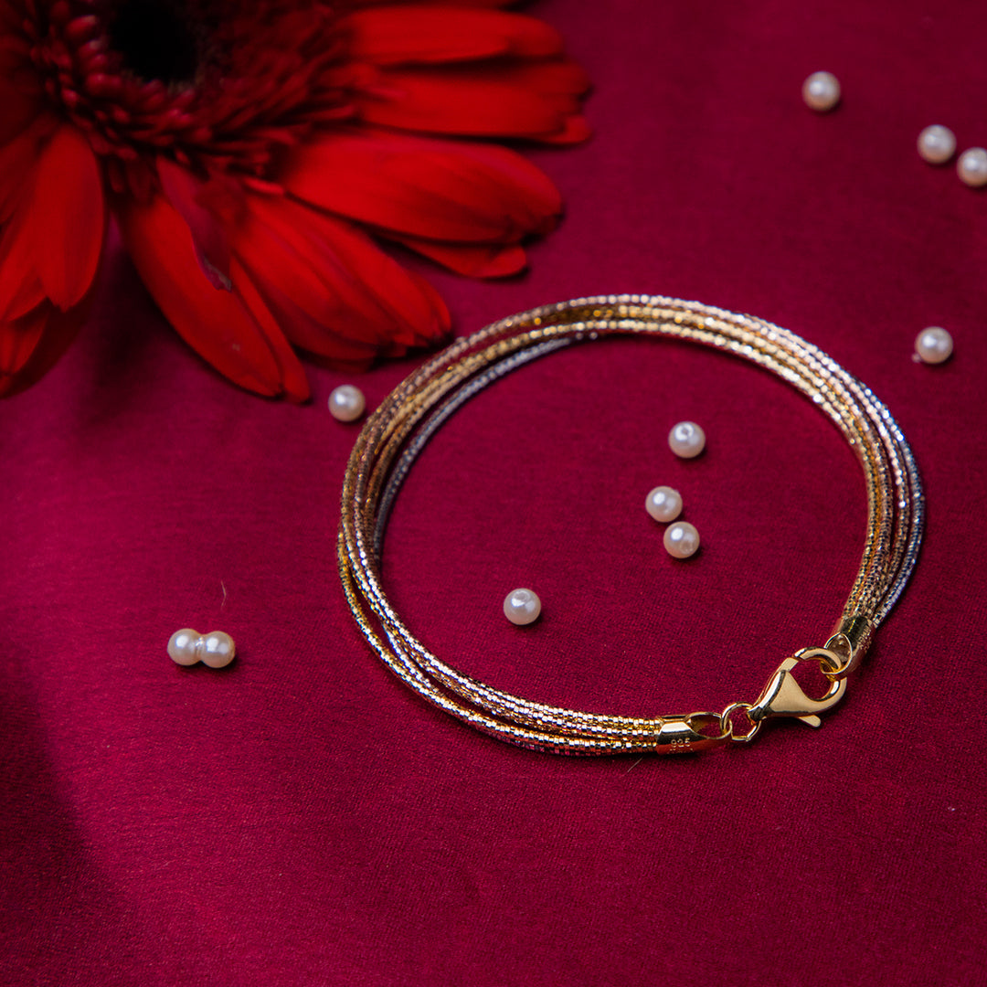 A sterling silver bracelet with a 5-layered design, featuring silver, rose gold and gold colors, displayed on a red background with a few pearls scattered around.