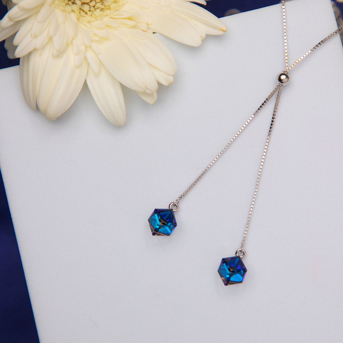 A sterling silver pendant chain with two blue azure stones, displayed on a white surface with a flower and a book in the background.