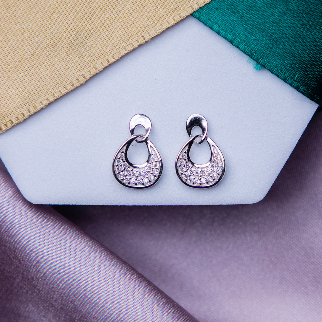 A pair of silver embellished earrings displayed on a white backkground with green and beige ribbon.