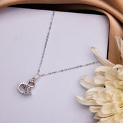 A silver pendant chain necklace with a swan-shaped pendant with dancing stone, displayed on a white surface next to a flower.