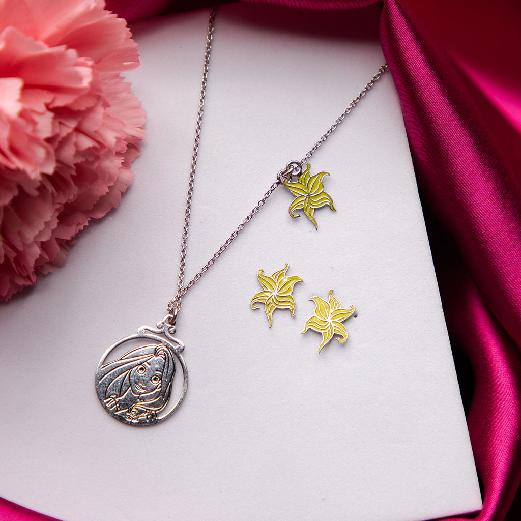 A sterling silver pendant set featuring a character from the Disney film 'Tangled', accompanied by a matching pair of earrings with floral motifs, displayed on a white surface with a pink flower and red fabric in the background.