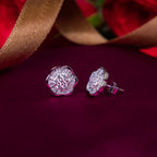 A pair of sterling silver stud earrings with a rhodium-based anti-tarnish coating, displayed on a magenta pink surface with a golden ribbon in the background.