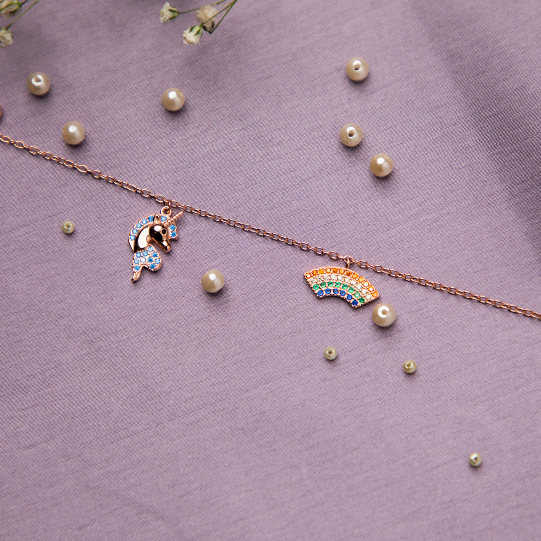 A sterling silver charm bracelet with rose golden and multi-colored charms, including a unicorn and a rainbow, displayed on a purple background with pearl accents.