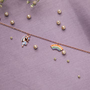 A sterling silver charm bracelet with rose golden and multi-colored charms, including a unicorn and a rainbow, displayed on a purple background with pearl accents.