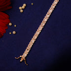 A tennis bracelet featuring a row of white stones set in a rose gold-colored bracelet, displayed against a dark background with a few pearls scattered around.
