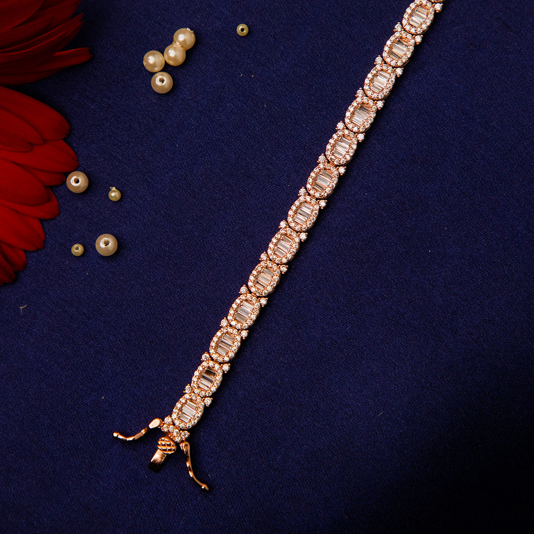 A tennis bracelet featuring a row of white stones set in a rose gold-colored bracelet, displayed against a dark background with a few pearls scattered around.