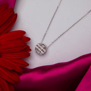 A sterling silver pendant chain with a round white stone pendant, displayed on a pink fabric surface with a red flower nearby.