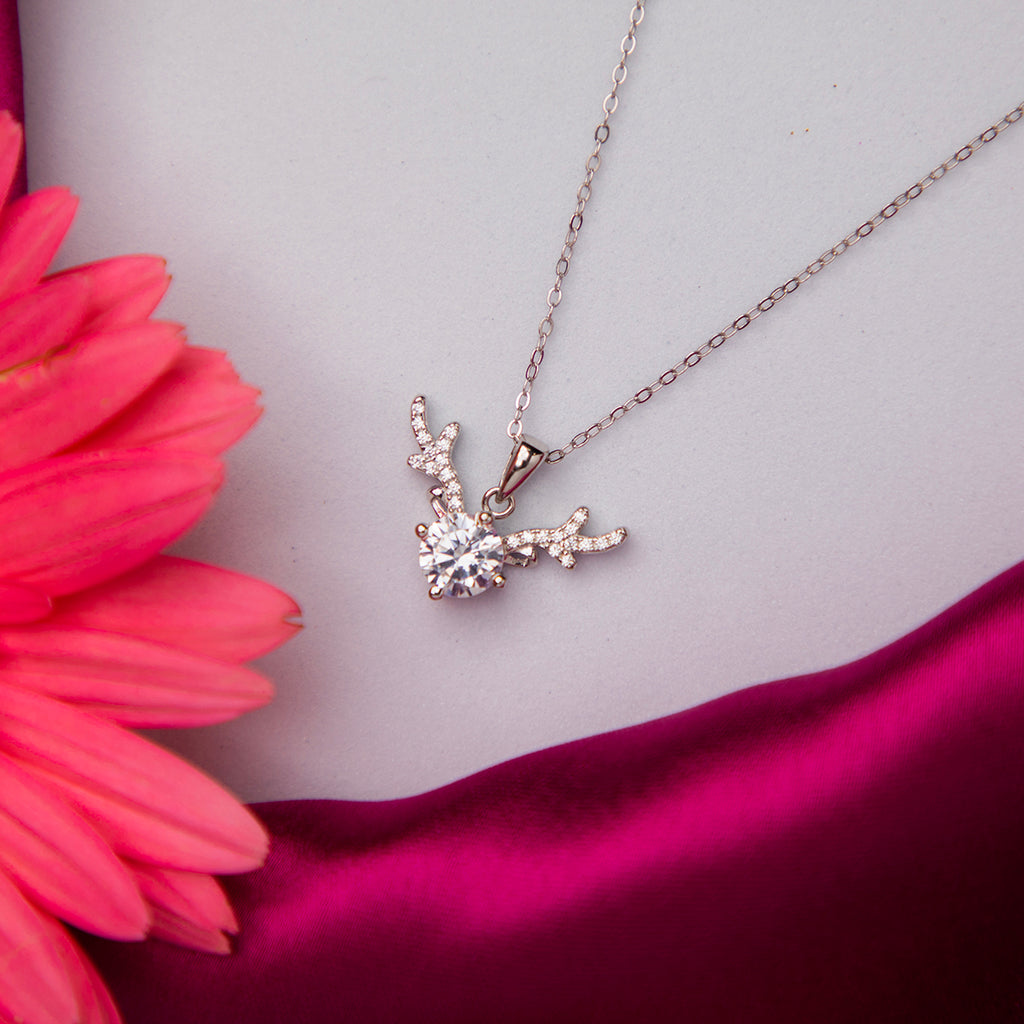 A silver pendant chain necklace with a reindeer antlers motif and a solitaire gemstone, displayed against a white and pink background.