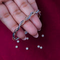 A sterling silver wire knot trendy bracelet held in a person's hand, with rose gold accents and silver beads scattered on a red background.