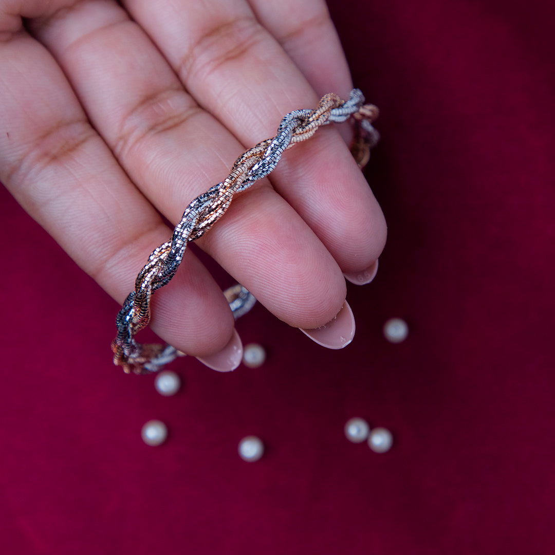 A sterling silver wire knot trendy bracelet held in a person's hand, with rose gold accents and silver beads scattered on a red background.