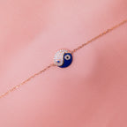 A sterling silver Yin-Yang charm bracelet with a rose gold finish and blue and clear accents on a pink background.