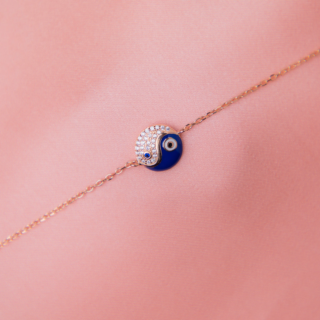A sterling silver Yin-Yang charm bracelet with a rose gold finish and blue and clear accents on a pink background.